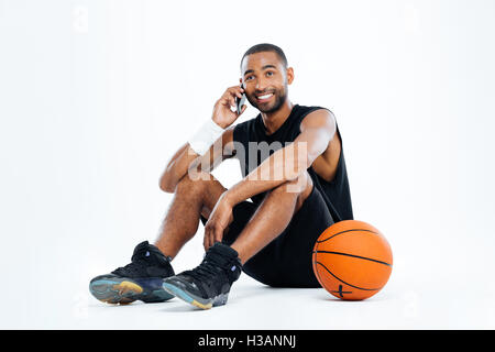 Glücklich Jüngling Basketball-Spieler sitzen und reden über Handy auf weißem Hintergrund Stockfoto