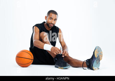 Hübscher junger Mann-Basketball-Spieler sitzen und Schnürsenkel binden, auf weißem Hintergrund Stockfoto