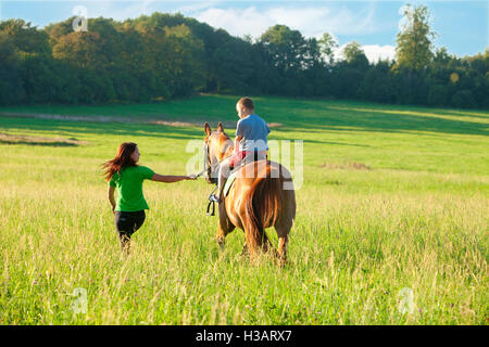 Reitstunden - Frau führt ein Pferd mit einem jungen im Sattel Stockfoto