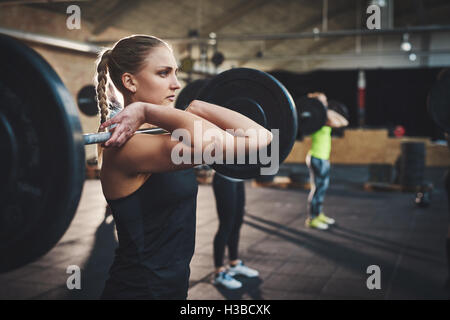 Taffe Frau mit dicken muskulösen Arme hochziehen große Hantel Fitness Training Klasse mit anderen Erwachsenen und schwarzer Boden Matten ich Stockfoto