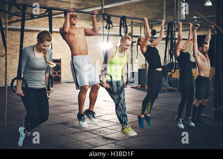 Gruppe von sechs jungen und starken männlichen und weiblichen Erwachsenen tun Chin ups mit Bar und Gurte im Cross fit Training gym Stockfoto