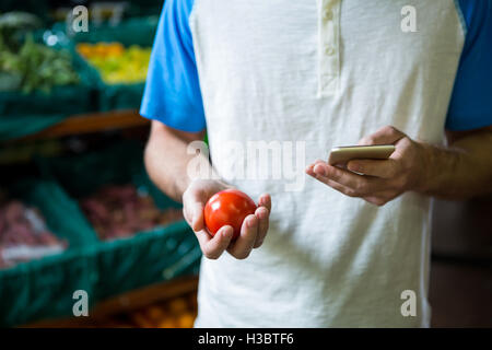 Mann hält Tomate und mit Telefon Stockfoto