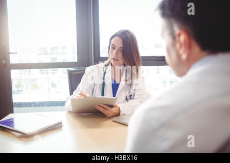 Ärztin, sitzt an ihrem Schreibtisch in Zwischenablage vor Patienten schreiben Stockfoto