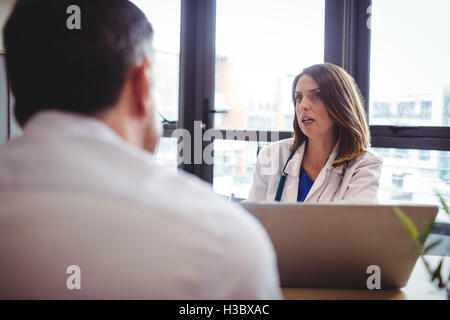 Ärztin, sitzt an seinem Schreibtisch im Gespräch mit Patienten Stockfoto