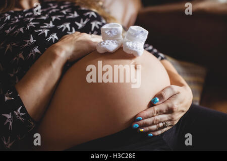 Baby Socken auf schwangeren Bauch im Wohnzimmer Stockfoto