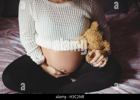 Schwangere Frau mit Teddybär im Schlafzimmer Stockfoto