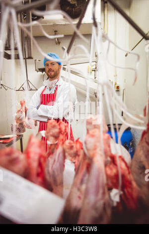 Porträt der Metzger Stand mit verschränkten in Fleisch-Lagerraum Stockfoto