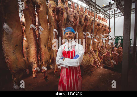 Porträt der Metzger Stand mit verschränkten in Fleisch-Lagerraum Stockfoto