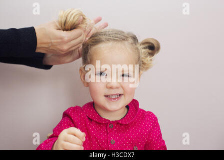 Kleine Mädchen, das ihr Haar in Zöpfen angeordnet Stockfoto