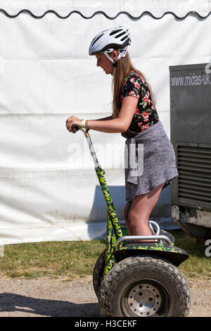 Junge Frau trägt einen Schutzhelm, Reiten einen Stand up zwei-Rad-Elektro-Roller, Musikfestival, Jimmys Farm, Ipswich, UK Stockfoto