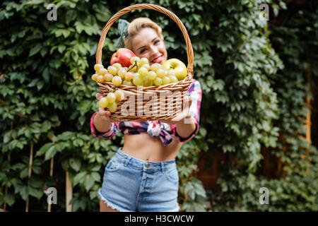 Lächelnd attraktive Pin-up Girl bietet und Ihnen Korb mit Früchten im freien Stockfoto