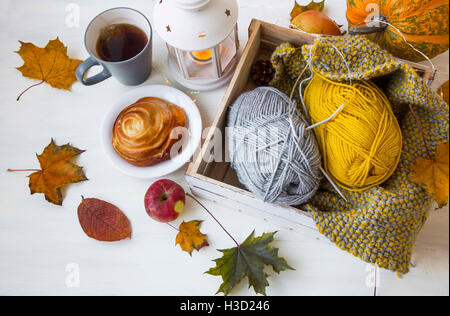 Gemütlichen Herbst Dekor mit Tee, Zimtschnecke, Laterne, Blätter, stricken Wolle und Nadeln, Licht und Kürbis auf weißen hölzernen staatlich Stockfoto