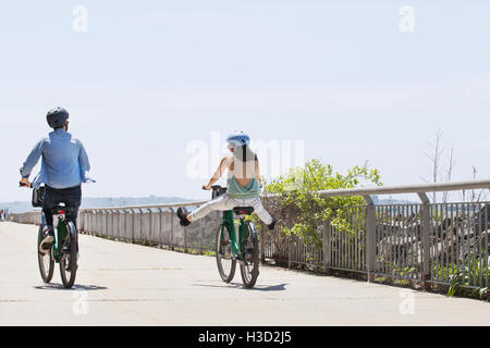 Ansicht der Rückseite des Paares auf dem Fahrrad über Promenade gegen den klaren Himmel Stockfoto