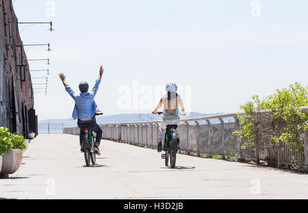 Ansicht der Rückseite des Paares auf dem Fahrrad über Promenade an einem sonnigen Tag Stockfoto