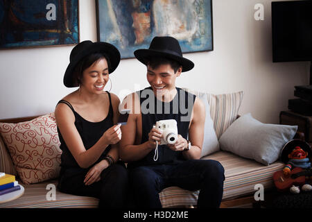 Glücklicher Mann hält Sofortbild-Kamera beim Fotografieren mit Frau im Wohnzimmer betrachten Stockfoto