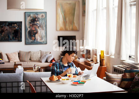 Junger Mann mit Laptop beim Kaffeetrinken zu Hause Stockfoto