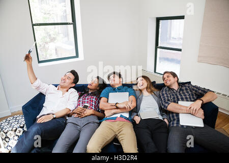 Fröhliche Geschäftsleute nehmen Selfie liegen auf Sofa im Kreativbüro Stockfoto