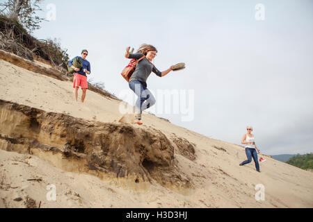 Frau Sprung von Sanddüne und genießen Sie mit Freunden am Strand Stockfoto