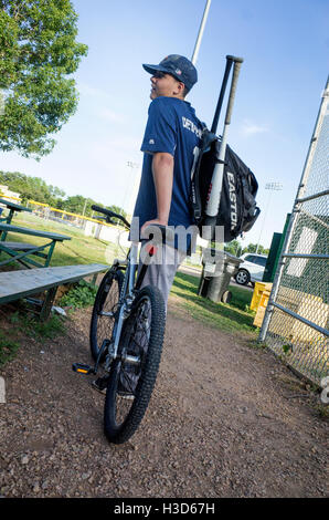 Junge Teen Baseballspieler in Uniform tragen zwei Fledermäuse mit seinem Fahrrad als Transportmittel. St Paul Minnesota MN USA Stockfoto