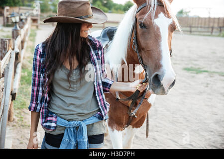 Smilng schöne junge Frau Cowgirl mit ihrem Pferd im Dorf Stockfoto