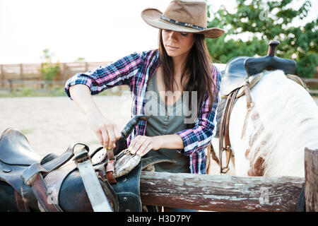 Hübsche junge Frau Cowgirl Hut arbeiten und Vorbereiten der Pferd Sattel Stockfoto