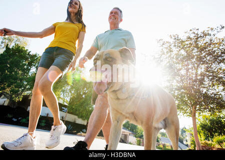 Älteres Paar in kurzen Hosen zu Fuß ihren Hund entlang einer Straße in der Sonne. Stockfoto