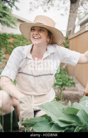 Eine Frau in einem Hut mit breiter Krempe Stroh arbeiten in einem Garten, graben. Stockfoto