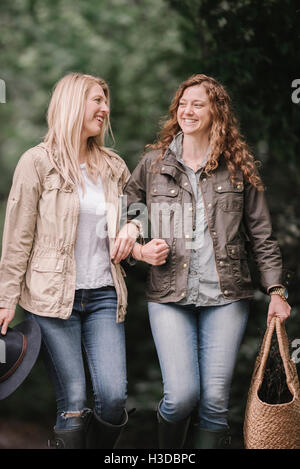 Zwei Frauen arm in Arm gehen in Mänteln und Stiefeln entlang einem Feldweg mit einem Korb. Stockfoto