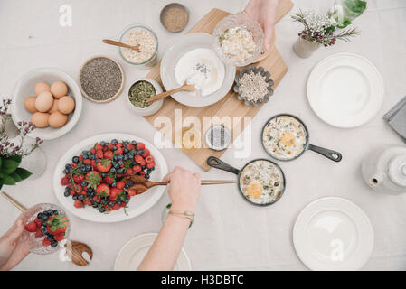 Draufsicht auf einen Tisch mit Speisen in Gerichten.  Frühstück, Beeren und Joghurt, Eiern und Brot. Stockfoto