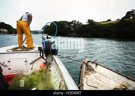 Ein Fischer in Watvögel auf einem Boot schleppen sich die Anker. Stockfoto