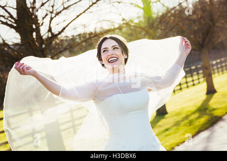 Eine Braut in ihrem Hochzeitskleid Lachen und streckte ihren Schleier hinter ihr, an ihrem Hochzeitstag. Stockfoto