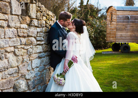 Eine Braut und Bräutigam küssen am Tag ihrer Hochzeit in einem Garten stehen. Stockfoto