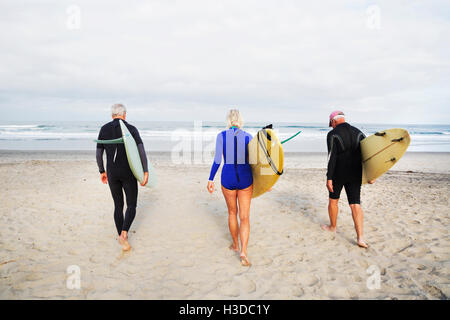 Ältere Frau und zwei alte Männer an einem Strand mit Neoprenanzügen und Surfbretter. Stockfoto