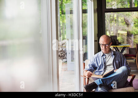 Ein Mann sitzt an einem Fenster, ein Buch zu lesen.  Unscharfen Vordergrund. Stockfoto