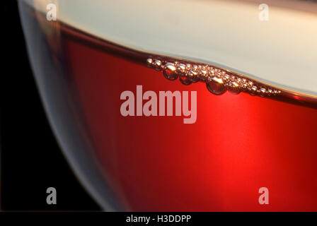 In einem frisch gegossenen, belüftetem Glas Rotwein bilden sich Luftblasen, die von der untergehenden Sonne beleuchtet werden Stockfoto