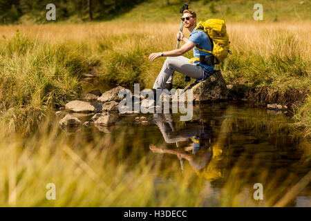 Junge Wanderer sitzen und ruhen neben einem Bergfluss Stockfoto