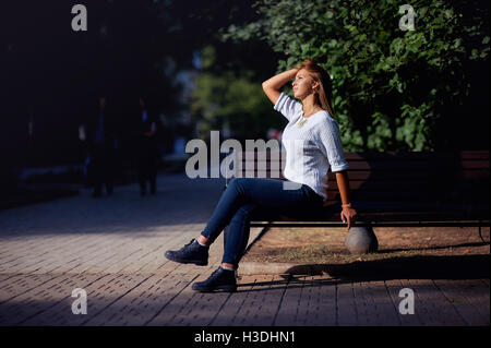 Schöne junge Frau sitzt auf einer Bank im Sommerpark Stockfoto