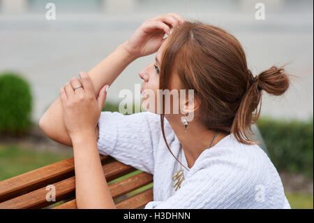 Schöne junge Frau sitzt auf einer Bank im Sommerpark Stockfoto