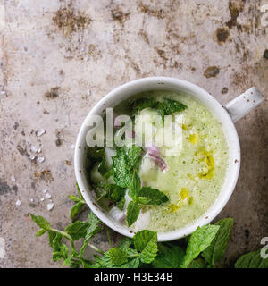 Keramische Tasse Gurken Gazpacho kalte Suppe mit Minze, Zwiebeln und Olivenöl, gedient mit Zutaten über alte Eisen-Hintergrund mit Stockfoto