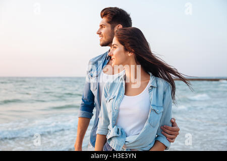 Glückliches junges Paar stehend und mit Blick auf das Meer am Strand Stockfoto