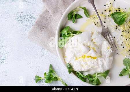 Italienische Käse Burrata mit Vintage Gabel, frischen Mais Salat, Sprossen und Olivenöl in weißen Keramikplatte auf Textile Napki geschnitten Stockfoto