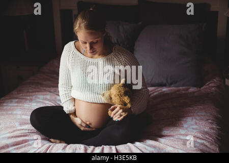 Schwangere Frau mit Teddybär im Schlafzimmer Stockfoto