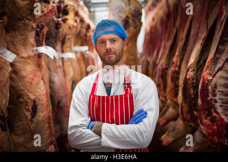 Porträt der Metzger Stand mit verschränkten in Fleisch-Lagerraum Stockfoto