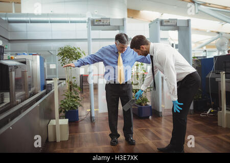 Flughafen Sicherheitsoffizier mit einer Hand hielt Metalldetektor einen Passagier zu überprüfen Stockfoto