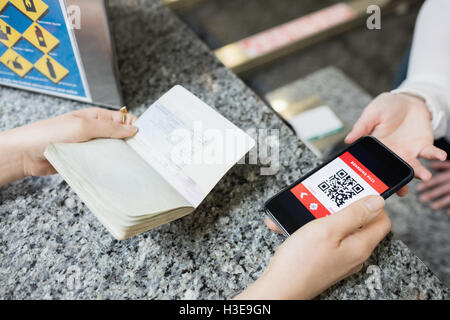 Passagier geben einen Reisepass und ein Handy an einer Fluggesellschaft einchecken Telefonzentrale Stockfoto