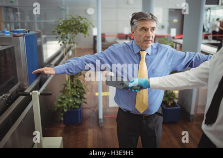 Flughafen Sicherheitsoffizier mit einer Hand hielt Metalldetektor einen Passagier zu überprüfen Stockfoto