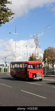 Roter Eindecker-City-Sightseeing-Bus auf der Oxford Street, Belfast, Nordirland mit der Skulptur Beacon of Hope im Hintergrund. Stockfoto