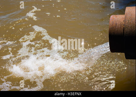 Wasser fließt aus rostigem Metall Düker Abflussrohr öffnen und Spritzwasser in braune Wasser schaumig schlagen. Stockfoto