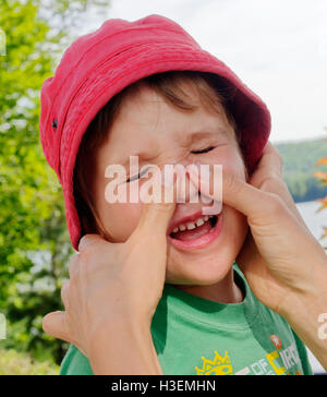 Ein Junge (4 Jahre alt) widerwillig mit Sonnencreme auf seinem Gesicht durch seine Mutter gelegt Stockfoto