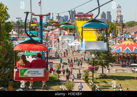 Die Menschen genießen Attraktionen und Fahrgeschäfte auf der Midway von der Ohio State Fair, mit der Skyline im Hintergrund in Columbus, Ohio. Stockfoto